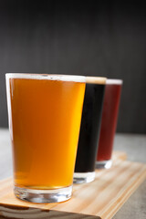 Three pint glasses of beer over wooden board. Golden, dark and red beer.