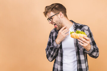 Handsome young man refusing unhealthy sandwich isolated over beige background. Diet concept. With...