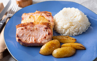 Pork stakes with pineapple, rice and potatoes over blue plate