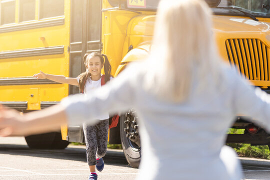 Kids Student Running Into Mother's Hands To Hug Her After Back To School Near The School Bus