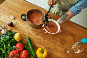 Close up of hands of man pouring tasty soup from pot into bowl. Italian cook preparing traditional meal in the kitchen. Cooking at home, Italian cuisine