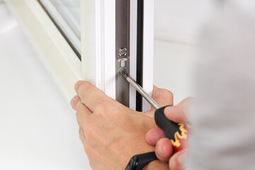 handyman adjusting white pvc plastic window indoors. worker using screwdriver to repair upvc window. homework maintenance