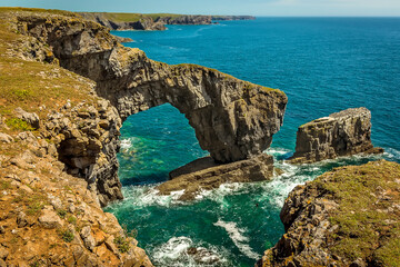 A dramatic natural rock arch called the Green Bridge of Wales and rock pillars on the south west coast of Pembrokeshire near Castlemartin in early summer