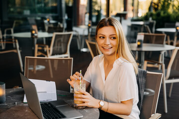 Young cheerful woman holding a glass of ice coffee at a cafe terrace. Coffee break concept.