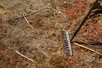 An old rake is on a dry meadow with a lot of dry earth in summer in Sicily