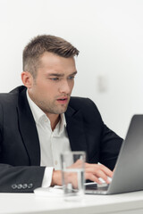 A handsome young guy in a business suit works in a car sales office. Online store in a laptop