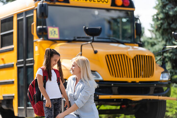 Mother brings her daughter to school near the school bus. back to school