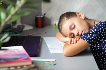 Distance learning online. The girl fell asleep on the table in front of the computer. Homeschooling during quarantine and coronavirus outbreaks. Boring home education