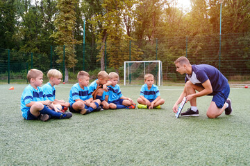 Young coach teaches little children the strategy of playing on football field.
