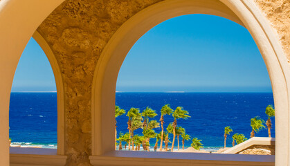 beautiful summer view of the blue sea and palm trees through the arch
