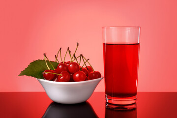 Glass of fresh cherry juice and some fresh cherries in bowl against bright red background.