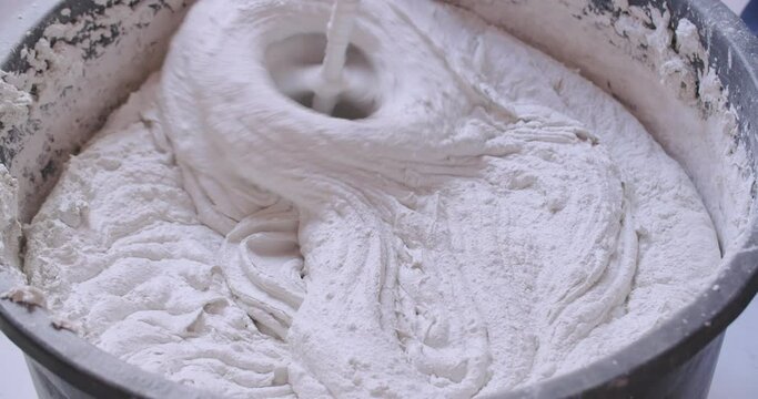 Closeup shot of a handheld mixer mixing plaster in a bucket.