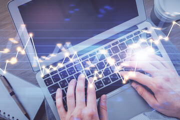 Double exposure of man's hands typing over computer keyboard and forex graph hologram drawing. Top view. Financial markets concept.