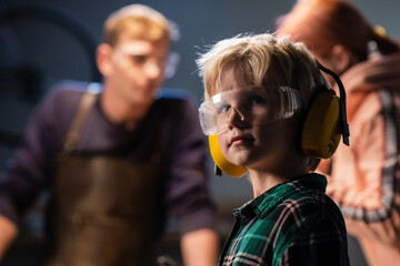 a boy with his father and mother in a carpenter's workshop in protective glasses and headphones, portrait