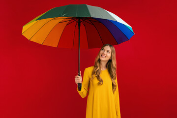 Happy young woman with a rainbow umbrella, on a red background