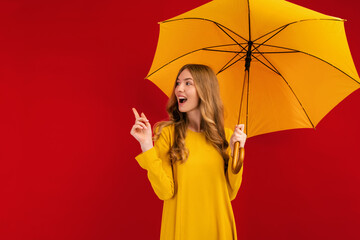 Shocked happy beautiful young woman, with a yellow umbrella on a red background