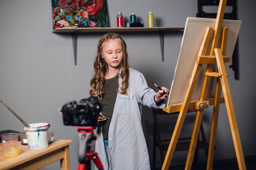 a cute teen artist is recording a story for her video blog in a workshop at an art school