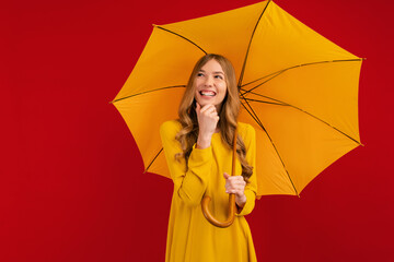 Happy thoughtful young woman with a yellow umbrella on a red background