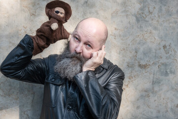 Portrait of a crazy artist puppeteer with beard, holding a robber doll in front of his eye, copy...