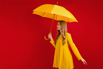 Beautiful happy young woman with yellow umbrella on red background, autumn concept