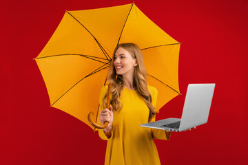 Happy beautiful young woman with a parasol using the laptop on a red background