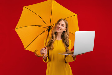 Happy beautiful young woman with a parasol using the laptop on a red background