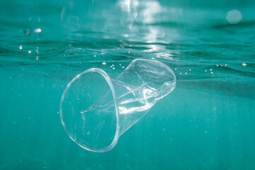 Plastic cup floats underwater in the open ocean. Environmental pollution concept.