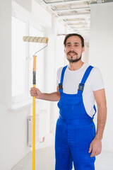 The repairman holds a roller in his hand, looks at the camera and smiles