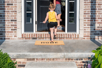 Barefoot little girl entering the front door of a home with a welcome mat that says Feels Good to be Home