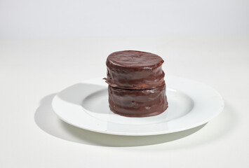 Typical Argentine chocolate alfajores filled with dulce de leche on a white plate on white background