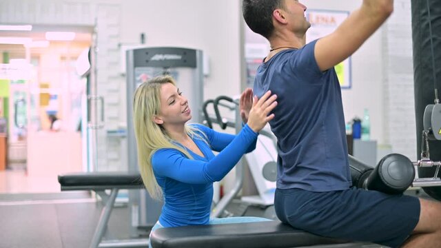Young woman trainer monitors the correctness of the exercise by the client of the fitness club