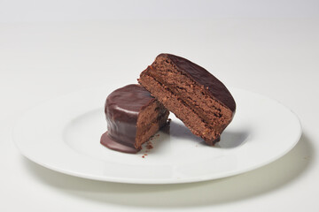 Typical Argentine Alfajor of dark chocolate cut in the middle where you can see the interior of chocolate and the filling of dulce de leche on a plate.