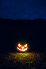 Glowing scary Halloween pumpkin on the grass at night, outdoor. Vertical orientation, copy space.