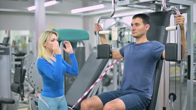 The trainer tells the client a skinny guy how to do the exercise on the exercise machine