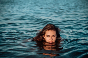 Beautiful young woman swiming in sea at sunset.