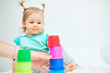 The child puts colorful toys with her mother in a pile on the bed