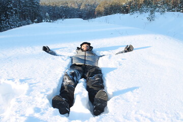 Fototapeta na wymiar Young man lying in snow with the forest in the background