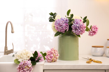 Bouquet with beautiful hydrangea flowers in can and scissors on light countertop