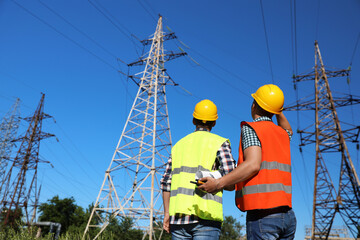 Professional electricians in uniforms near high voltage towers