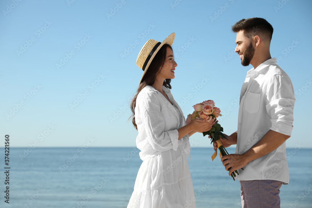 Wall mural Young man giving flowers to his wife at beach. Honeymoon trip