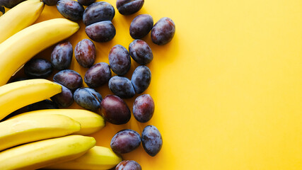 Fresh fruits background. Bananas and purple plums on yellow background, copy space. Healthy food concept.