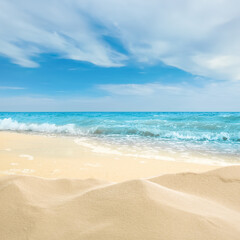 Fototapeta na wymiar Ocean waves rolling on sandy beach under blue sky with clouds