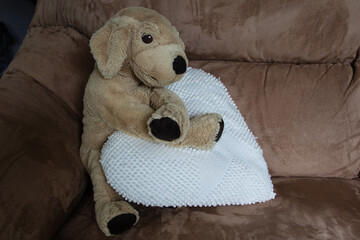 A cute and cuddly stuffed animal puppy sitting on a beige couch with a white heart pillow
