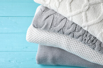Stack of folded warm sweaters on turquoise wooden background, closeup