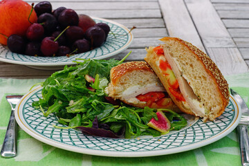A turkey and tomato sandwich on brioche bun with green salad