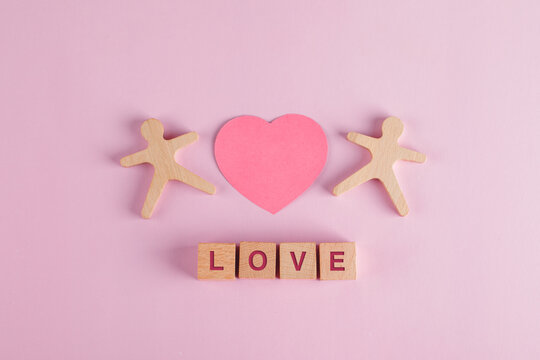 Relationship concept with paper cut heart, wooden cubes, human models on pink background flat lay.