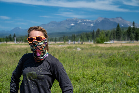 Cute, wholesome adult woman with braided hear poses in a meadow in Polebridge Montana. Neck gaiter (face mask) during COVID-19 pandemic