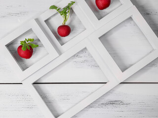 Three radishes are arranged in a white wooden frame lying on a white table. Close-up top view.