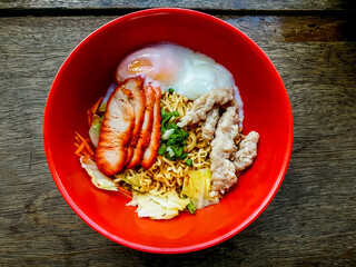 Dry egg noodles with pork, mince pork and boil egg in red bowl on the wood table.