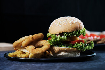 Burgers with cheese, salads and vegetables on a black background wooden board.
